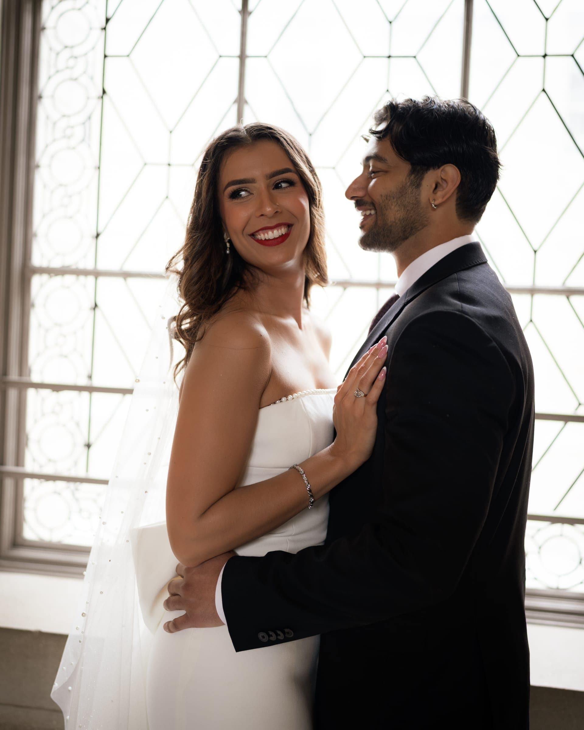 Anna smiling in Bishal's arms by a leaded-glass window
